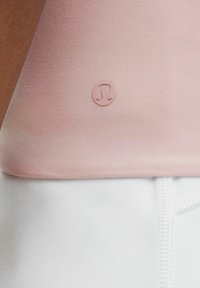 Light pink athletic top made of smooth fabric; features a small, raised logo in the center. Bottom hem aligns with white shorts.