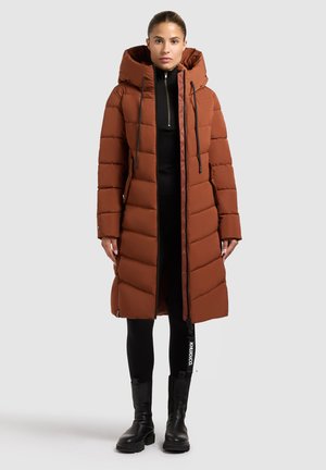 Long, padded brown coat with a hood, featuring a front zipper, drawstrings, and two side pockets. Worn over a black top and leggings.