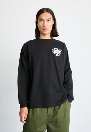 Černá dlouhá rukávová košile s kulatým výstřihem, na levé hrudi s bílým logem ve tvaru plamene. Spárováno s olivově zelenými kalhotami.