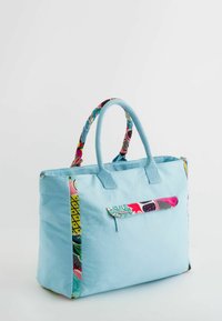 Bolsa de tela de color azul claro con acentos de patrones coloridos en los lados, dobles asas y un bolsillo delantero. Textura y diseño distintivos.