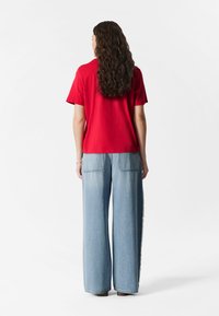 Rotes Baumwoll-T-Shirt mit kurzen Ärmeln, kombiniert mit hellblauen weiten Jeans mit zwei Gesäßtaschen und geradem Saum.