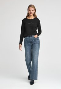 Schwarzes Langarmshirt mit "Polo Club"-Schriftzug, kombiniert mit hellblauen weit geschnittenen Jeans und schwarzen Stiefeletten. Einfaches und lässiges Design.