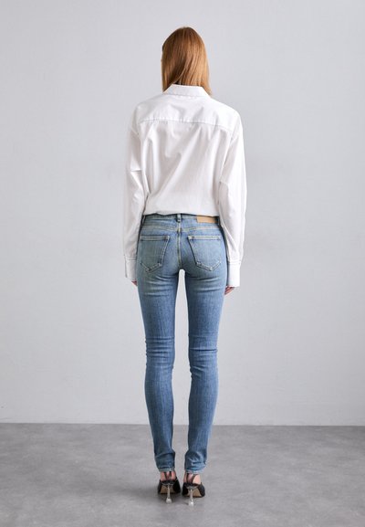 Cămașă albă cu mânecă lungă, asortată cu blugi skinny de culoare albastru deschis. Blugii au talie medie și buzunare clasice la spate. Tocuri negre completează ținuta.