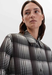 Camicia a bottoni in bianco e nero con motivi a griglia intrecciati. Presenta un colletto classico e una consistenza della stoffa liscia e leggera.