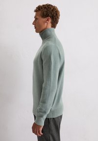 Jasnozielony, dopasowany sweter z wysokim kołnierzem, wykonany z miękkiego materiału. Rybacze mankiety i dół, gładka faktura oraz minimalistyczny design.