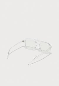 Lunettes de soleil rectangulaires transparentes avec des montures claires et des verres vert clair, présentant des branches fines et un design minimaliste.