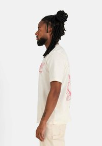 Crème-kleurig T-shirt met korte mouwen, voorzien van een rode bloemenprint aan de voor- en achterkant, met een ontspannen pasvorm en een zachte textuur.