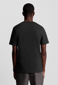 Svart bomulls T-shirt med korta ärmar, rundad halsringning och slät textur. Inga synliga logotyper eller mönster, visad bakifrån.