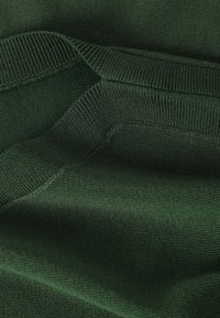 Donkergroen gebreide stof met gedetailleerde geribbelde en gladde texturen, met nadruk op naden en plooien.