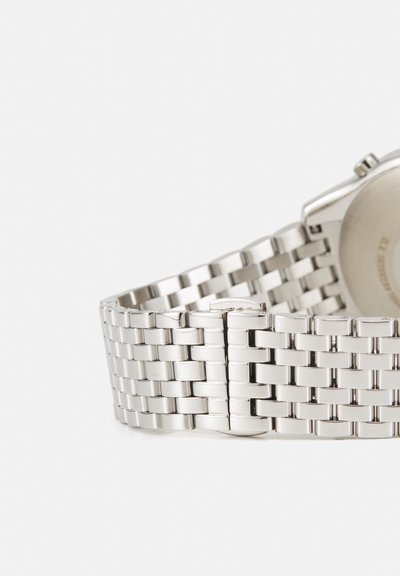 Silbernes Metalluhrenarmband mit verbundenen rechteckigen Segmenten und einem geschlossenen Verschluss, vor einem schlichten hellen Hintergrund positioniert.