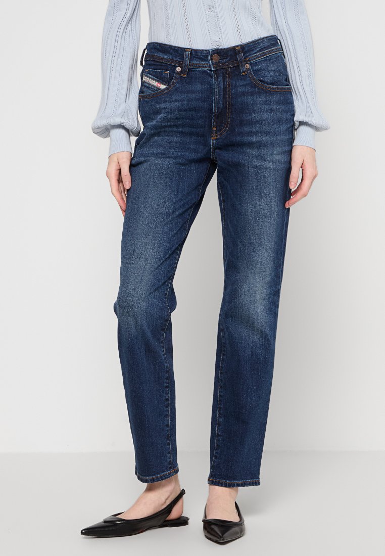 Jeans blu scuro a gamba dritta con chiusura a bottone, cinque tasche, leggera scoloritura e cuciture a contrasto. Indossati con un maglione chiaro e ballerine nere.