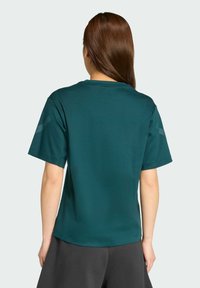 Tyrkysové tričko s krátkym rukávom vyrobené z mäkkej tkaniny, s okrúhlym výstrihom a jemnými akcentmi na pleciach. Skombinované s voľnými čiernymi šortkami.