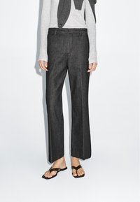 Donkergrijze broek met een rechte pijpdesign, met een soepel stoffen textuur en voorste plooidetails. Gepaard met een lichte trui en platte sandalen.