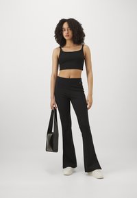 Svart crop top med tunna axelband, matchad med svarta högmidjade utsvängda byxor. En liten svart handväska och vita sneakers fulländar outfiten.