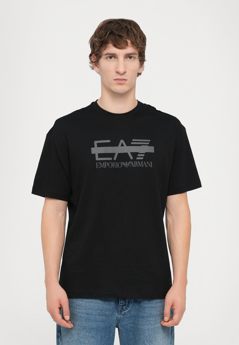Black cotton t-shirt with a round neckline, featuring a gray graphic logo design "EA7 EMPORIO ARMANI" printed across the front. Short sleeves.
