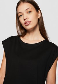 Svart t-skjorte med korte ermer, rund halslinning og løs passer. Mykt stoff med en jevn tekstur som fremhever en enkel design.