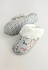 Grå slippers med hvide, fluffy manchetter og trykte dachshundhunde, hvor den ene slipper viser en rippelsole med teksten "relax".