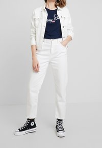 Bílá džínová bunda přes námořnické tričko s textem, bílé džíny s vysokým pasem a černé vysoké tenisky s bílou podrážkou a logem.