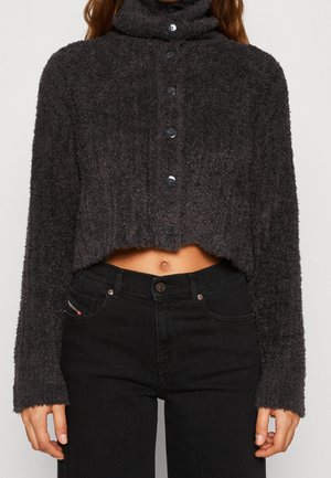 Pull court boutonné doux gris foncé à manches longues, associé à un jean noir taille haute, laissant apparaître une petite partie du ventre.