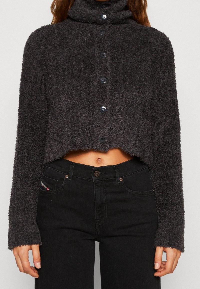 Pull court boutonné doux gris foncé à manches longues, associé à un jean noir taille haute, laissant apparaître une petite partie du ventre.