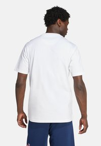 T-shirt en coton blanc à manches courtes, col rond et coupe décontractée. Détail de couture visible le long du col et de l'ourlet.
