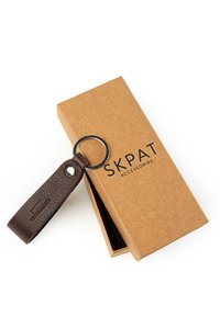Llavero de cuero marrón con superficie texturizada, unido a un anillo metálico, colocado junto a una caja de cartón marrón lisa con la etiqueta "SKPAT ACCESSORIES".