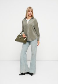 Zielona koszula z kordurowego materiału na guziki, jasnoniebieskie spodnie w stylu wide-leg oraz ciemnozielona torebka z akcentem w kształcie gwiazdki. Gładkie tekstury i luźny krój.