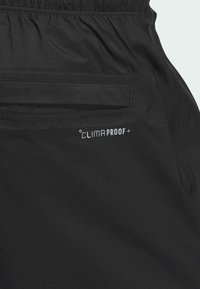 Czarny, lekki materiał o teksturowanej powierzchni. Posiada elastyczną talię, boczną kieszeń oraz biały napis "CLIMAPROOF+".