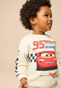 Sudadera blanca con un gráfico rojo de Lightning McQueen, texto que dice "95 El legendario Lightning McQueen," y diseño de mangas a cuadros.