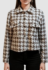 Chaqueta de pata de gallo en marrón y blanco con cierre de botones en la parte delantera, dos bolsillos en el pecho y cuello. Tejido suave y texturizado.