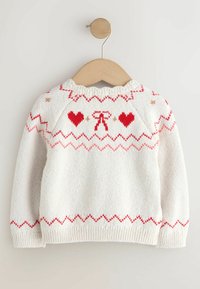 White knitted sweater with red hearts and zigzag patterns. Features a ribbed crew neckline and cuffs. Hangs on a wooden hanger.