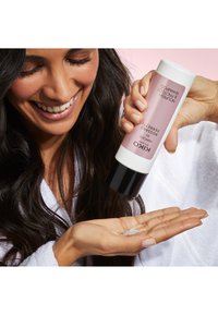 KIKO Nourishing and Perfecting-schampo i ett rosa rör med svarta detaljer, som doserar en ljus, krämig konsistens i en öppen handflata.