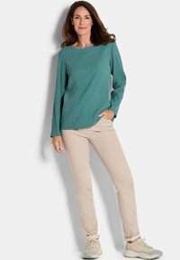 Teal Longsleeve-Oberteil mit gerippter Textur, kombiniert mit hellbeigen Slim-Fit-Hosen und gedämpften Sneakers, präsentiert in einer frontalen Haltung.