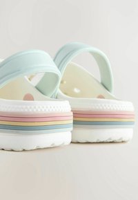Sandales à plateforme blanches avec des brides bleu pastel et des semelles rayées multicolores en rose, jaune, vert et bleu.