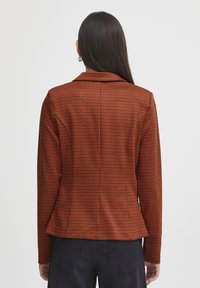 Op maat gemaakte blazer in een oranje en zwart geruit patroon, met een notch-kraag en een getailleerd silhouet met een peplumzoom. Soepele stofstructuur.