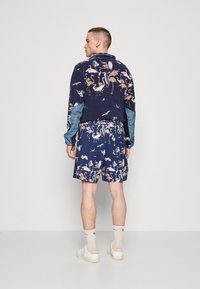 Mørkeblå klessett med et mønstret skjorte og shorts med flamingo-design. Laget av et mykt stoff med en avslappet passform.