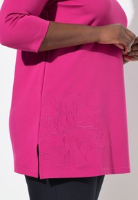 Top fucsia con maniche a tre quarti, caratterizzato da un design ricamato floreale all'orlo e fessure laterali per un tocco in più.