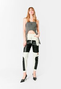 Top corto gris con un logotipo redondo, combinado con pantalones de cintura alta en piel sintética negra y crema, que cuentan con cierre frontal y cortes laterales.