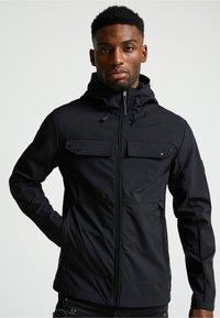 Melnā ūdensizturīgā jaka ar kapuci, ar rāvējslēdzēja priekšējām kabatām, rāvējslēdzēja aizdari un regulējamiem kabeļiem ap apkakli.