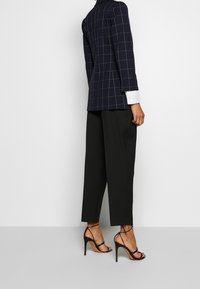 Marinblå rutigt blazer med långa ärmar, parat med svarta byxor. Svarta sandaletter med hög klack fulländar outfiten.