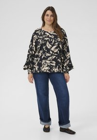 Blouse à motif noir et crème avec une coupe ample et des manches ballon, associée à un jean en denim bleu à jambes larges et des ballerines noires.
