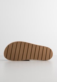 Sole of a shoe, brown rubber with vertical ridges, rounded toe, embossed logo, flat profile, textured surface for grip.
