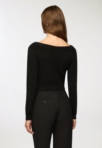 Czarny sweter z dzianiny o odkrytych ramionach i długich rękawach, o teksturowanej tkaninie, w połączeniu z czarnymi spodniami o wysokim stanem z tylnymi kieszeniami.