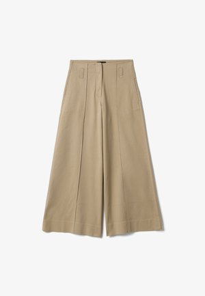 Beige wijde broek met voorste naden, ceintuurlussen en zijzakken, plat gelegd op een witte achtergrond.