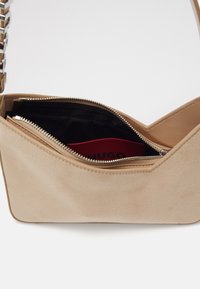 Beige svineders håndtaske med lynlås, der har et sort indre og et rødt logo-tags. Sølv hardware pryder stroppen.