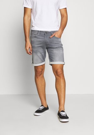 Shorts de mezclilla gris con dobladillos enrollados, con un diseño clásico de cinco bolsillos y cierre de botones. Combinados con una camiseta blanca lisa y zapatillas negras.