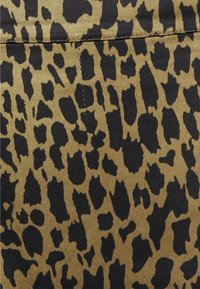 Tissu à imprimé léopard présentant des taches noires irrégulières sur un fond doré beige, avec une texture lisse et des coutures visibles.