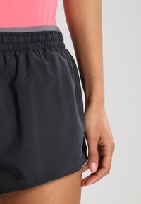 Czarne szorty z elastyczną talią, charakteryzujące się gładką teksturą i boczną kieszenią. Ich konstrukcja jest lekka i odpowiednia do użytku sportowego.