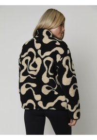 Veste en peluche noire et crème à motifs avec un col haut, dotée d'une texture douce et d'un design de tourbillon abstrait, idéale pour une tenue décontractée.