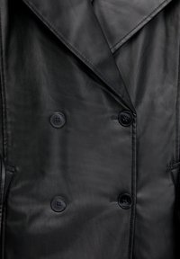 Veste en cuir noire à double boutonnage avec quatre boutons et grands revers, présentant des coutures surpiquées et des poches latérales.